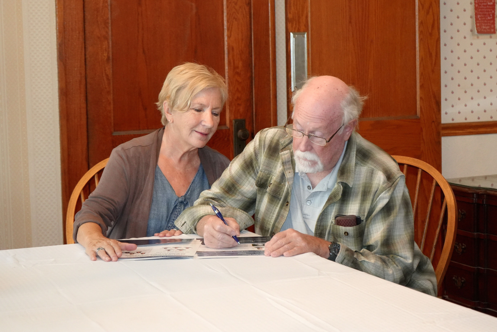 Older couple reviewing paperwork together at their dining room table while planning their retirement move.