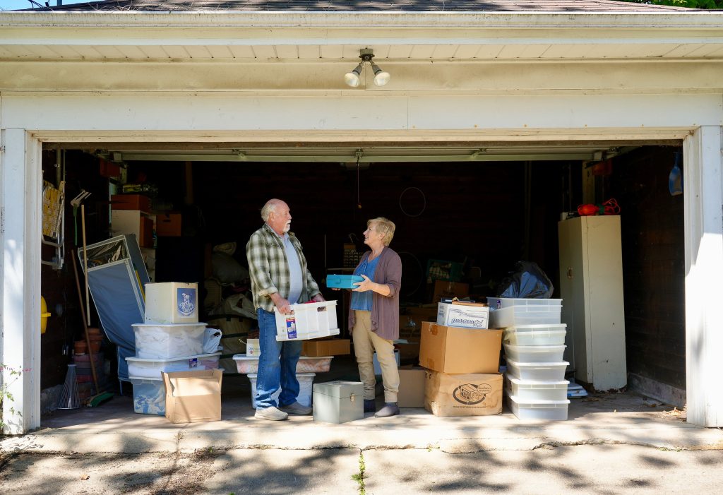 Older couple sorting storage bins and belongings in their garage while preparing to downsize their home.