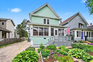 Two-story light green house with an enclosed front porch, landscaped garden, and driveway.